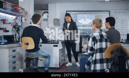 L'insegnante sta spiegando i principi del lavoro con la mano robotica, mostrando esempi sul grande schermo della Modern University. Gli adolescenti fanno brainstorming e fanno domande. Concetto di ingegneria robotica. Foto Stock