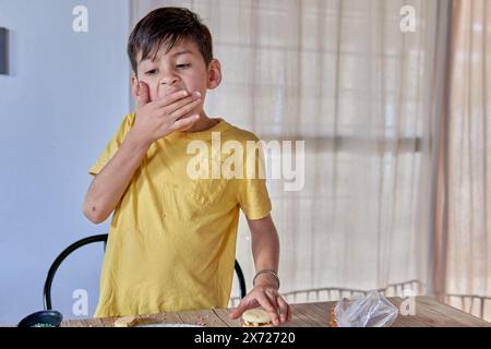 ragazzo latino in maglietta gialla mangiando sprinkles mentre cucinava alfajores de maicena a casa Foto Stock