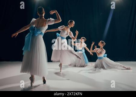 Quattro giovani ballerini in tuto bianco etereo e fasce blu, che si posano elegantemente su un palco poco illuminato. Coreografia Foto Stock