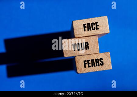 Affronta le tue paure parole scritte su blocchi di legno con sfondo blu. Il concetto affronta il simbolo delle tue paure. Copia spazio. Foto Stock