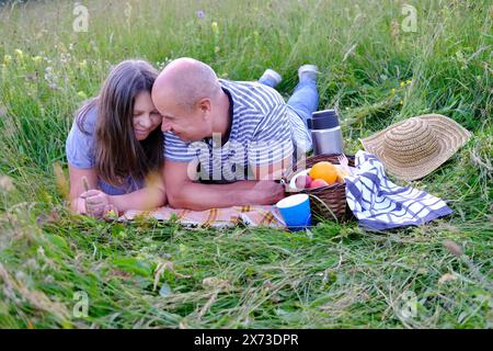 uomo maturo 60 anni, donna 50 anni in abiti blu giace sull'erba nel prato, accanto al cestino da picnic con frutta, thermos con tè, concetto di fam Foto Stock