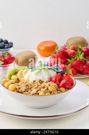 Muesli con fragole, kiwi, banana e mirtilli in un piatto rotondo con yogurt sul tavolo. Cibo sano e gustoso Foto Stock