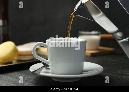 Versare il caffè dalla moka alla tazza sul tavolo con texture scure, primo piano Foto Stock