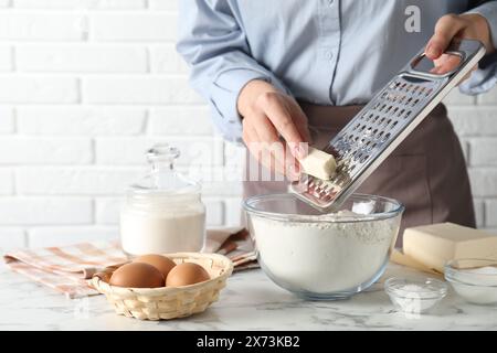 Donna che grattugia il burro nel recipiente con la farina al tavolo di marmo bianco, primo piano Foto Stock