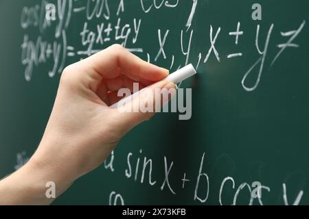 Insegnante che scrive l'equazione matematica sulla tavola verde, primo piano Foto Stock