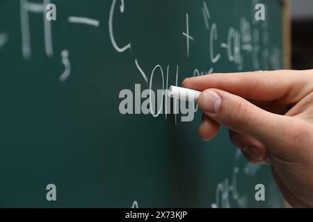 Insegnante che scrive formule chimiche con gesso su lavagna verde, primo piano Foto Stock