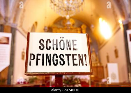 17 maggio 2024: Auguri di felice Pentecoste di Whitsun, scritta su un cartello di fronte ad un altare nella chiesa. FOTOMONTAGGIO *** Schöne Pfingsten Pfingstgrüße, Schriftzug auf einem Schild vor einem Altar in der Kirche. FOTOMONTAGE Foto Stock