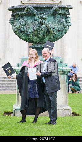 Una studentessa laureata, in abito accademico, dell'Università di Cambridge, in Inghilterra, celebra il suo successo accademico con suo padre sul prato della camera del Senato, di fronte alla gigantesca urna graeco, venerdì 17 maggio 2024. Foto Stock