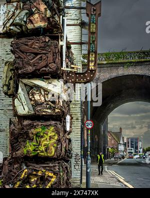 Strada secondaria urbana interna con un alto ponte ad arco ferroviario, una persona che cammina in strada e muro di auto schiacciate e cielo spettacolare Foto Stock