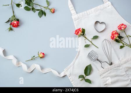 Accessori da forno con grembiule con rose di fiori su sfondo grigio, piatto, vista dall'alto. Ricette di cottura natalizie Foto Stock