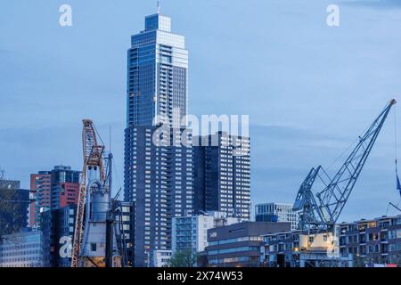 Grandi e moderni grattacieli e gru da cantiere dominano la vista serale della città, piccolo porto in una grande città con un faro e. Foto Stock