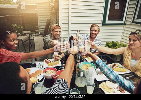 Amici, brindisi e pranzo alla festa, sul cortile o felici per cibo, diversità o festeggiamenti sul patio. Persone, uomini e donne con bevande, alcolici o birra Foto Stock
