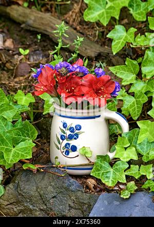 Una natura morta di fiori di Giglio di San Martino e fiori di Statice viola. In un piccolo vaso. Su un muro con ivy. Foto Stock