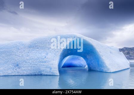 Un grande blocco di ghiaccio blu con un buco che galleggia nel lago Argentino. Foto Stock