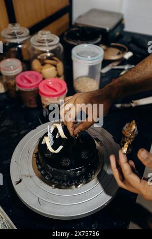 Primo piano di uno chef maschile irriconoscibile che decora la torta al cioccolato con frutta candita nella sua cucina. Foto Stock