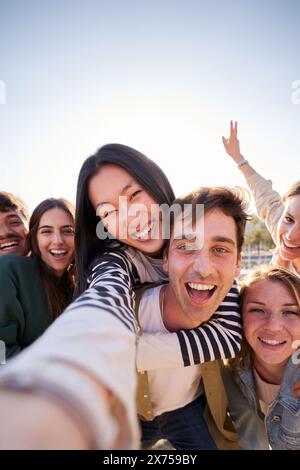 Raggruppa un giovane amico felice che scatta selfie insieme, sorridendo alla fotocamera. Gente di Piggyback. Foto Stock