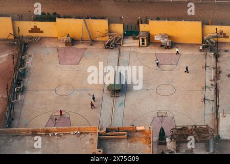 Vista aerea di una scuola di cemento al Cairo con numerosi campi da pallacanestro e giochi per bambini, circondata da pareti gialle e attrezzature minime. Foto Stock