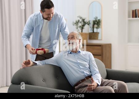 Figlio che regala una confezione regalo a suo padre a casa Foto Stock