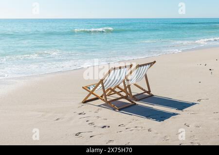 Sulla spiaggia, due sedie vuote si affacciano sull'oceano su una spiaggia sabbiosa Foto Stock