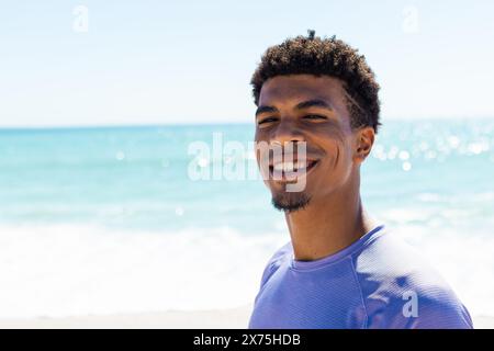 In spiaggia, giovane uomo birazziale in piedi, sorridente alla macchina fotografica, copia spazio Foto Stock