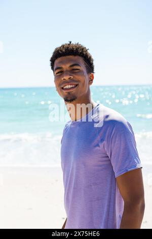 In spiaggia, giovane birazziale sorridente, con una camicia blu Foto Stock