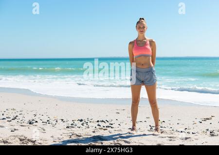 In spiaggia, giovane donna caucasica in piedi, mani sui fianchi Foto Stock