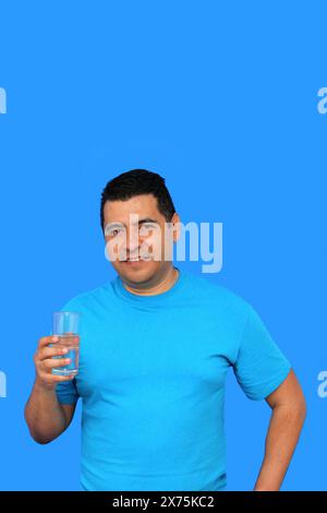 Un uomo latino dalla pelle scura mostra il suo bicchiere con acqua ferma per idratarsi quando fa caldo Foto Stock