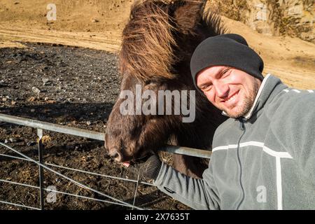 Film turistico scatta selfie al rallentatore con un bellissimo cavallo islandese bianco dietro la recinzione isolato nella giornata di sole in Islanda. Scopri i momenti di viaggio più belli Foto Stock