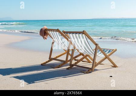 In spiaggia, sedia vuota con cappello sulla spiaggia sabbiosa, onde dolci che toccano la spiaggia Foto Stock