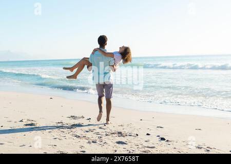 In spiaggia, coppia birazziale che si diverte insieme, uomo che trasporta una donna Foto Stock