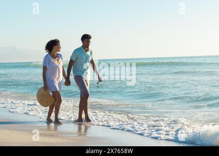 In spiaggia, coppia birazziale che si tiene per mano, cammina Foto Stock