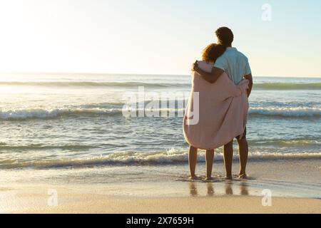 In spiaggia, diverse coppie in piedi, avvolte in coperta, che guardano il mare Foto Stock