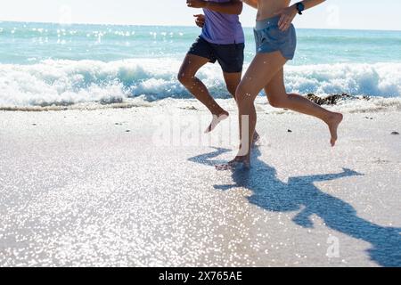 In spiaggia, diverse coppie che corrono, onde che toccano i piedi Foto Stock