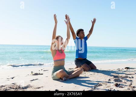 In spiaggia, coppie diverse che praticano yoga, entrambe alzando le braccia Foto Stock