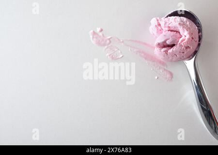 Paletta per gelato in metallo con paletta per fragole isolata su un tavolo bianco colorato con gelato. Vista dall'alto. Foto Stock