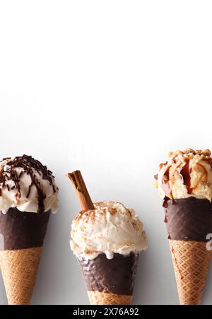 Dettaglio di tre coni di gelato di vari gusti con coni di cioccolato su sfondo bianco. Composizione verticale Foto Stock