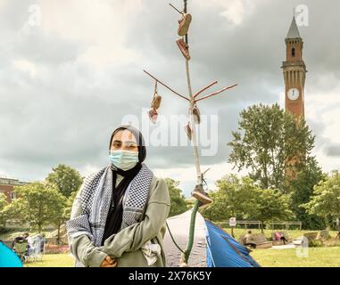 Uno studente che indossa una maschera facciale all'accampamento di protesta pro palestinese dell'Università di Birmingham. Vecchio Joe, la clocktower sullo sfondo. Foto Stock