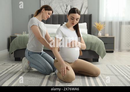 Doula massaggiava una donna incinta in camera da letto. Preparazione alla nascita del bambino Foto Stock