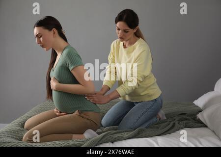 Doula massaggiava una donna incinta in camera da letto. Preparazione alla nascita del bambino Foto Stock