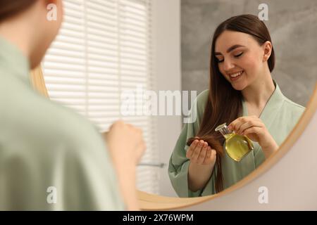 Giovane donna che applica la maschera per capelli a olio vicino allo specchio a casa Foto Stock
