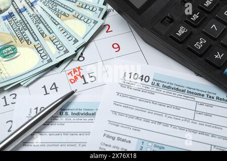 Giorno fiscale. Calendario con promemoria della data, documenti, banconote in dollari, penna e calcolatrice in tabella Foto Stock