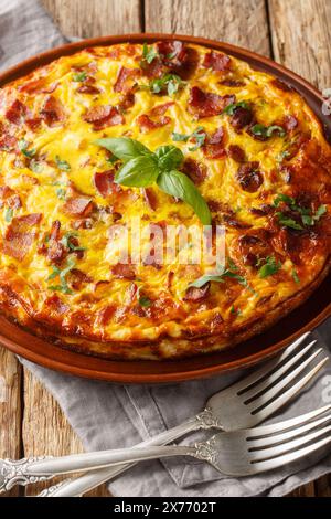 Quiche frittata senza crosta con pancetta, pollo e formaggio da vicino sul piatto sul tavolo di legno. Verticale Foto Stock