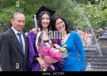 ORGOGLIO FAMILIARE. Dopo la cerimonia di laurea della NYU del 2024, una bella ragazza asiatica americana posa con i suoi genitori. Al Washington Square Park di Manhattan. Foto Stock