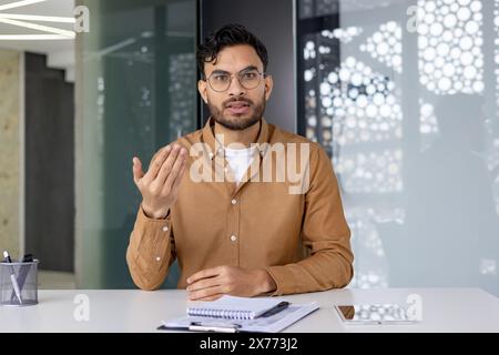 Uomo in ufficio che guarda la telecamera e spiega qualcosa seriamente. Concetto di riunione aziendale professionale. Foto Stock