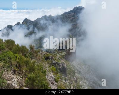 Vista dal Pico Ruivo, la vetta più alta di Madeira, Portogallo. Montagne verdi, nuvole nebbiose e oceano atlantico sul sentiero escursionistico PR1.2 da Achada do Foto Stock