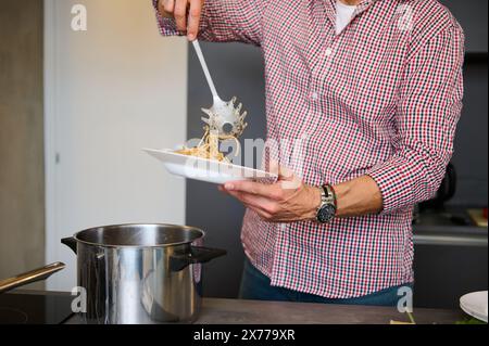 Primo piano, uno chef maschile che riversa il passato italiano appena cucinato in un piatto bianco, pronto a servirlo ai clienti. Consumismo di cibo e bevande. Cucina. E Foto Stock