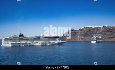 Una tradizionale barca a vela passa tra le gigantesche navi da crociera "Odyssey of the Seas" e "Norwegian Epic", al largo di Santorini. Foto Stock