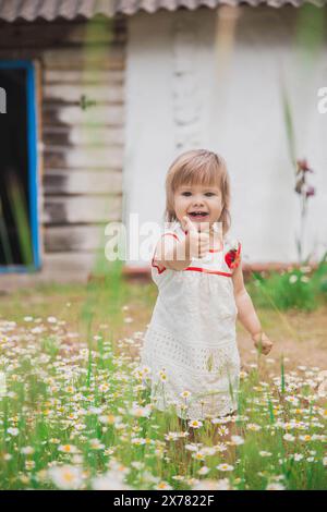 incantevole bambino in un abito ricamato vicino a una capanna di legno Foto Stock