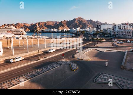 Ampia vista di un incrocio stradale costiero e del lungomare di Mascate, Oman, con montagne rocciose che si innalzano dietro la città e traffico leggero Foto Stock