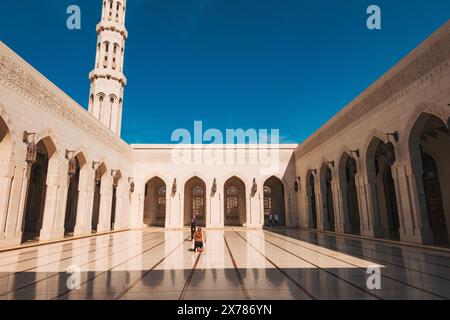 Vista dall'angolo basso del cortile della grande Moschea del Sultano Qaboos a Mascate, Oman. Presenta un alto minareto, archi in arenaria e pavimento in marmo lucido Low-an Foto Stock